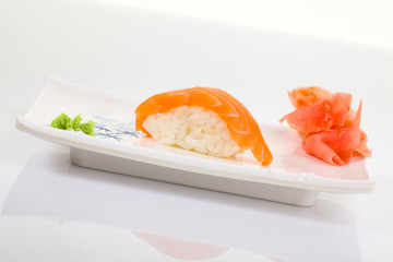 Japanese Cuisine - Appetizing Salmon Sushi Set. Philadelphia Sushi Roll - Maki Sushi with Philadelphia Cheese inside on mirror black background. Smoked salmon rolls served on a plate