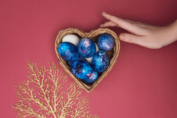  Happy Easter. Beautiful festive composition. Basket with Easter eggs, a female hand and a golden branch on a colorful background.