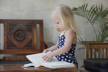 Candid portrait of adorable toddler girl with a book on a balcony during hot summer day