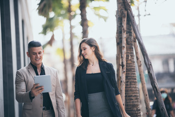 Happy businessman showing content on tablet to female colleague. Business man and woman walking outside