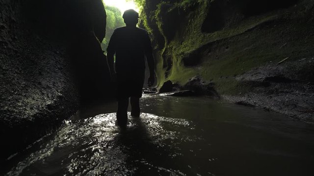 A man walks knee deep in river water in a canyon in the asian tropics UHD