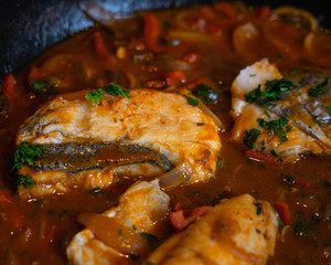 Hake fillet stew, cooking in a tomato sauce with red pepper sauce, with some parsley leaves to garnish