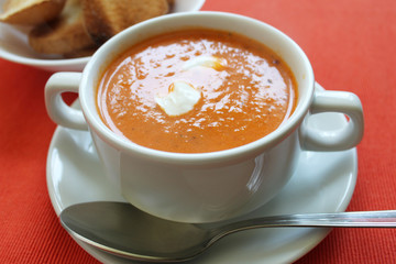 Tomato cream soup hot orange color close up view on bright red background. Selective focus. Copy space