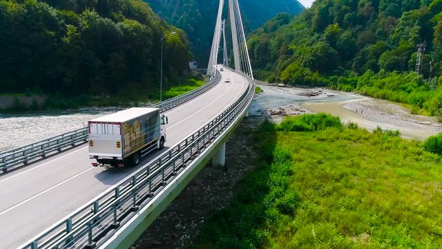 Truck crosses beautiful bridge in summer. Scene. Top view of truck carrying things driving across bridge on background of beautiful forest landscape. Travel and relocation