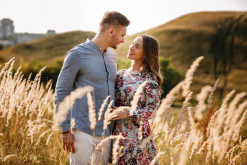 beautiful young couple hugging in a field with grass at sunset. stylish man and woman having fun outdoors. family concept. copy space.