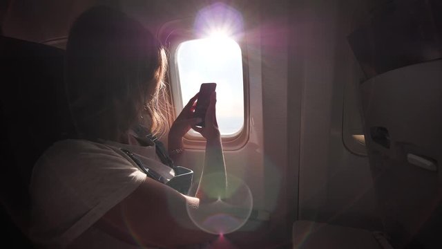 A girl takes pictures of beautiful landscapes from the airplane window using her phone.
