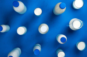 Collection of bottles and glasses with milk on blue background, top view