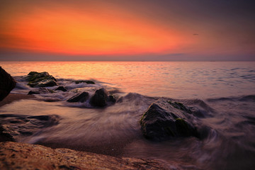 Obraz premium Sunrise at sea. Stones, waves and the sun. Seascape.