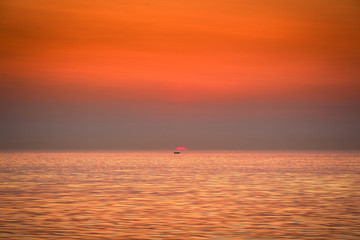 The boat is floating against the backdrop of the rising sun. Golden sunrise at sea.
