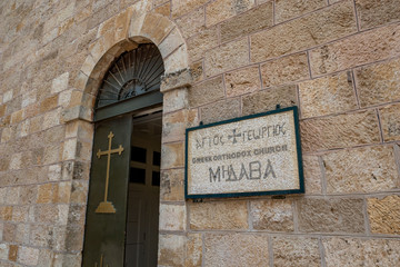 The beautiful mosaic plaque at the entrance of Saint George Greek orthodox church in Madaba, Jordan. Winter day street view with the open old door of the religious building
