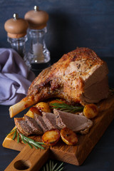 Roast leg of lamb with potatoes and rosemary on dark background. vertical image