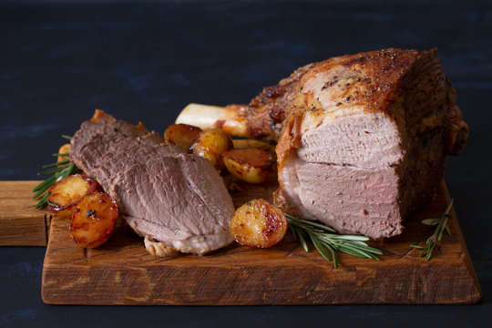 Roast leg of lamb with potatoes and rosemary on dark background. horizontal image