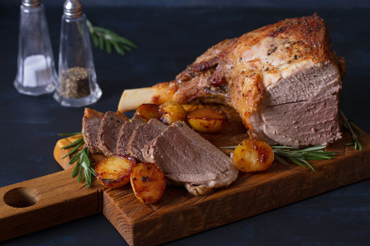 Roast leg of lamb with potatoes and rosemary on dark background. horizontal image