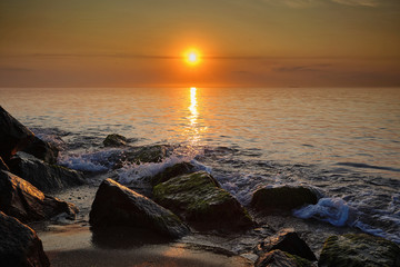 Sunrise at sea. Stones, waves and the sun. Seascape.