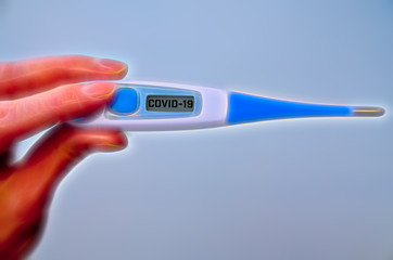 Female hand holds clinical thermometer with covid-19 text on the screen during global covid-19 or corona pandemic
