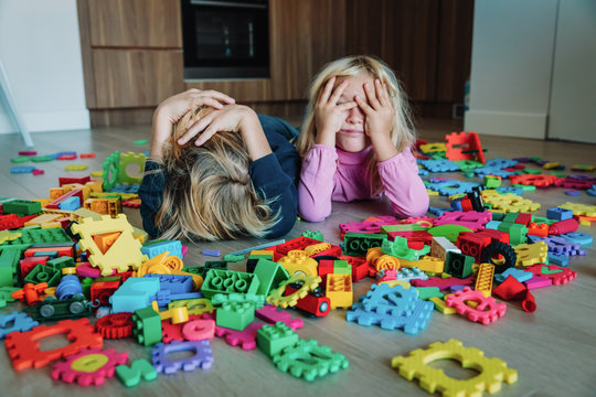 little boy and girl tired stressed exhausted with toys scattered indoors