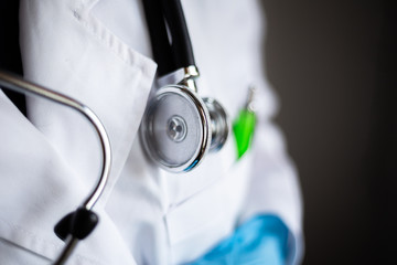 Closeup of a stethoscope head on a doctor's neck. White gown and a green pen in a medical worker pocket. Hospital stuff being used for check for coronavirus sars illness, doctor visit concept.