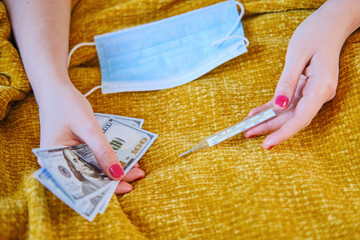 Women's hands hold dollars and a thermometer, a close-up mask. Money for treatment for coronavirus in America