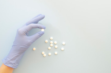 Female hand in a blue medical glove holds white round pills. Protection against virus, coronavirus, flu, colds, diseases. Traditional medical tool, concept of health. Medical background