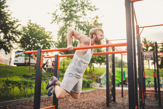 Fit Man Workout Out Arms On Dips Horizontal Bars Training Triceps And Biceps Doing Push Ups. Handsome Man Doing Exercise On Parallel Bars. Male Athlete Exercises On Parallel Bars Outdoor