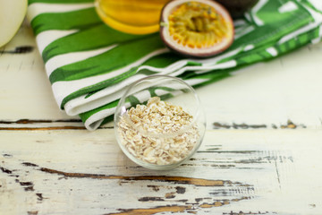 Flattened oats in a neat round glass bowl on an old beautiful table. Close-up. In the background is a beautiful towel, passion fruit and green tea.