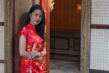 Portrait of Chinese girl wearing Chinese clothes holding paper folding fan in her hand and posing at cement door