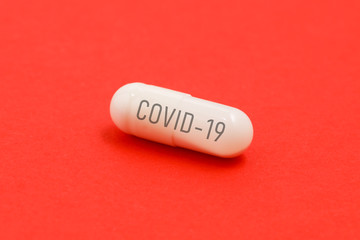 White capsule with the inscription COVID-19 on red surface, close up. edical concept of Virus Pandemic Protection, Coronavirus COVID-19