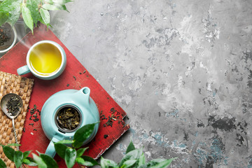 A cup of green tea in a blue cup on a gray concrete background. Cup of green tea with a teapot on a gray concrete background with copy space. Top view