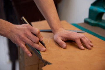Obraz na płótnie Canvas Cutting genuine leather with knife. Working process of leather craftsman. Close up of male hands and leather cutting.