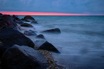 Obraz premium Sunrise at sea. Stones, waves and the sun. Seascape.