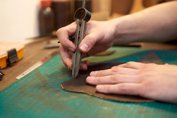Сloseup of the master measuring the width of the seam on natural leather using craft tools. The seam width measurement process.