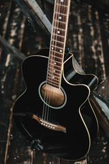 A black acoustic guitar stands in a room with a dark interior. Dark mood, loft, music, musical instrument.