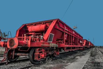 Fototapeta na wymiar Tren de mercancías de hierro en color rojo varado en una vía férrea. Tren parado en una estación de ferrocarril con cielo azul de fondo. 