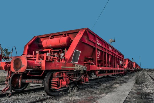 Tren de mercanc&iacute;as de hierro en color rojo varado en una v&iacute;a f&eacute;rrea. Tren parado en una estaci&oacute;n de ferrocarril con cielo azul de fondo. 