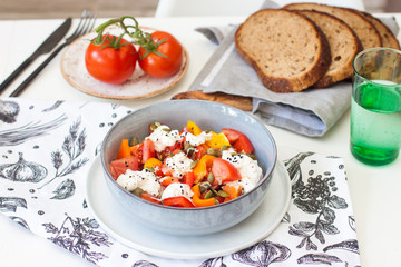 Salad bowl with chopped tomatoes, pepper, cream cheese, black sesame and pumpkin seeds