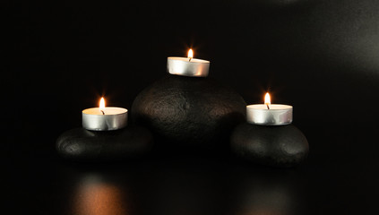 three black stones lie on a black background, candles are burning, close-up, reflection