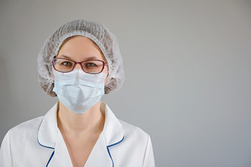 Medical worker portrait. Confident female doctor in protective face mask and eyeglasses on gray background.