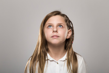Obraz premium Studio portrait of a cute girl with long blonde hair looking upside against neutral background