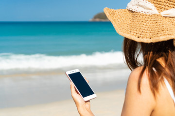 Fototapeta premium Happy traveller Asian woman enjoys at tropical beach while using smart phone on vacation. Summer on beach concept.