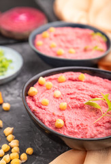Hummus with beet and microgreen basil sprouts in ceramic bowl on a black concrete background. Side view, selective focus.