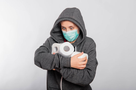 The concept of panic because of the coronavirus, a girl in a sweatshirt with a hood and a medical mask buys toilet paper. Studio photo on a white background.