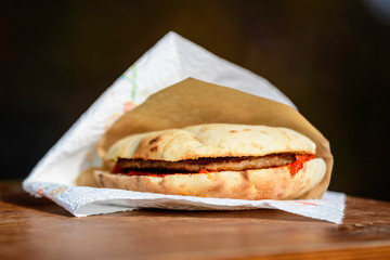 Tasty Pljeskavica sandwich, a traditional national Serbian dish with grilled dish of spiced meat patty mixture or pork, beef and lamb, served with red tomato sauce displayed on brown paper