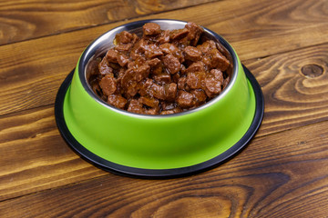 Canned food for cats or dogs in green metal bowl on wooden floor