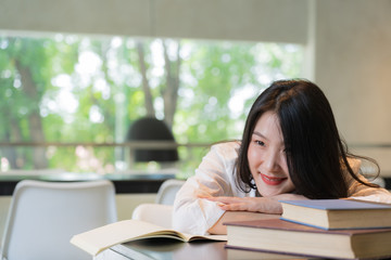 Beautiful student wearing white shirt resting while reading books on the table in library