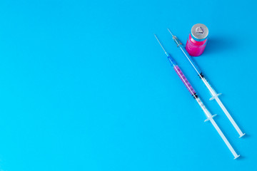 On a blue table are two insulin syringes filled with a drug of different colors, and next to it is an ampoule with a medicine for an injection for a disease. Healthcare concept