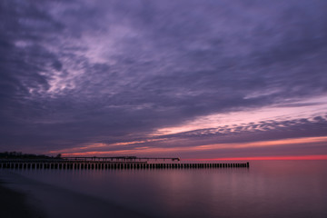 Fototapeta premium wooden groyne stakes at dawn with colorful evening sky