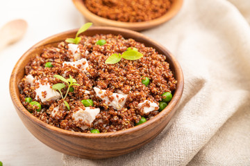 Quinoa porridge with green pea and chicken in wooden bowl on a white wooden background. Side view, selective focus.