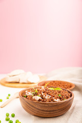 Quinoa porridge with green pea and chicken in wooden bowl on a white and pink background. Side view, selective focus, copy space.