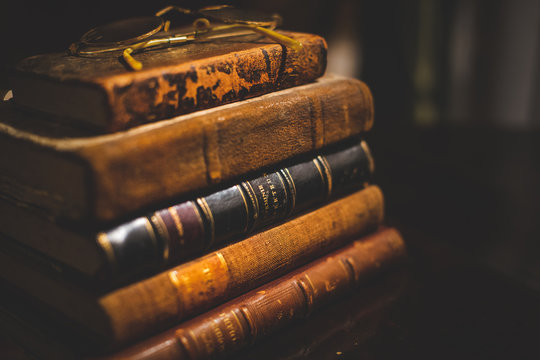 A vintage pile of five old brown leather books with eye glasses on a wood table.	