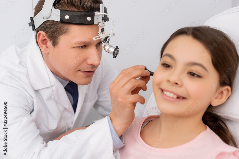 Wall mural attentive ent physician examining ear of cute child with ear speculum